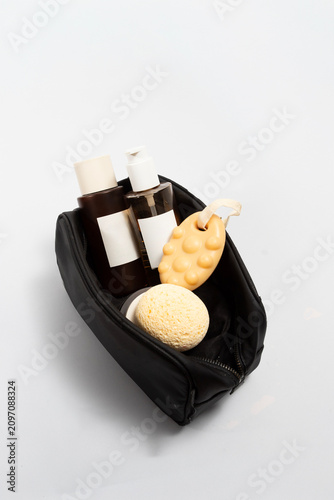 Skincare travel set. The black pouch neatly holds amber glass apothecary jars, solid shampoo and soft facial sponges, emphasizing a holistic and natural approach to travel wellness.