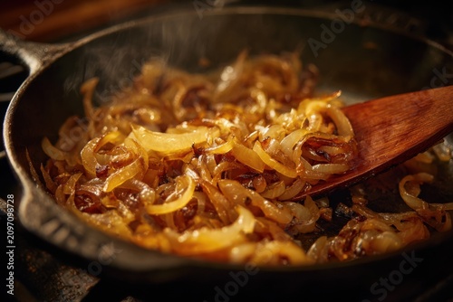 Action shot of caramelized onions being stirred in cast iron, golden-brown softened onions with caramelized edges