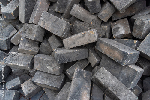 A dense pile of reclaimed rectangular dark gray clay paving bricks with worn edges, mortar residue and weathered surfaces. The construction material creates a detailed industrial texture for renovatio