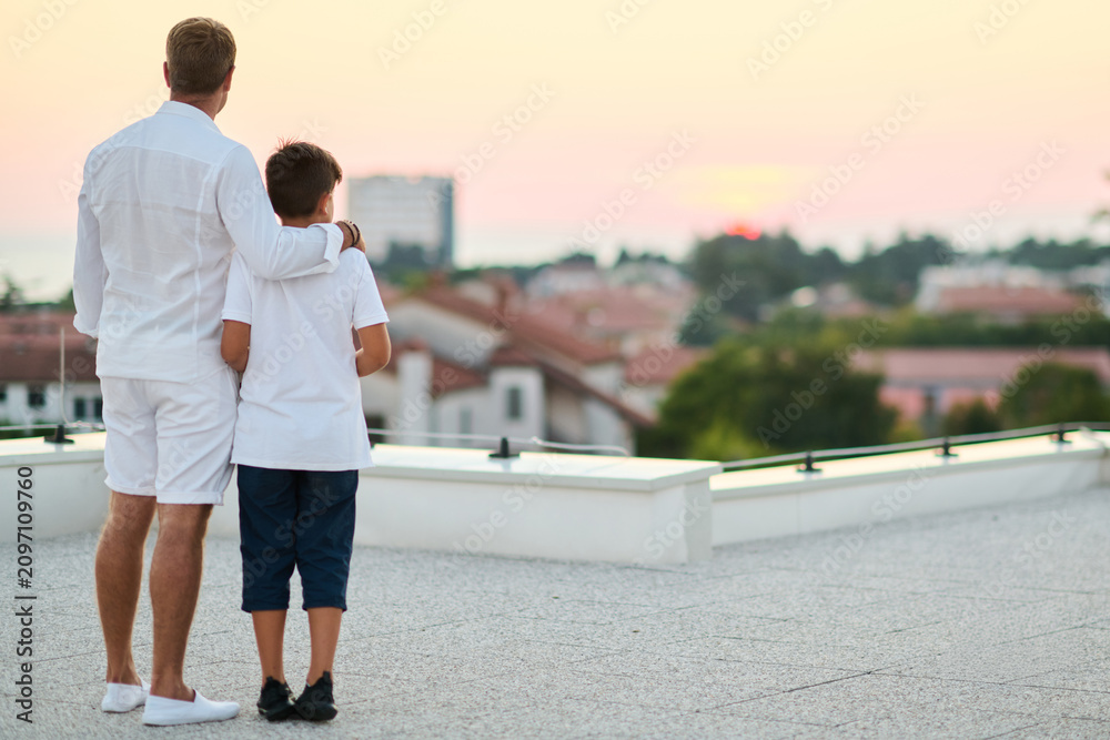 Obraz premium Father And Son On Rooftop Balcony Overlooking Sea View At Sunset Family Moment Together