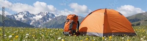 Summer camp tent and backpack set up in a mountain meadow with wildflowers