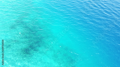Aerial top down view of turquoise to deep blue sea water texture with sun rays reflection