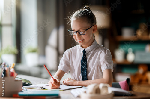 Quadro su tela Smiling Schoolgirl Studying at Home Desk, Wearing Glasses and Tie