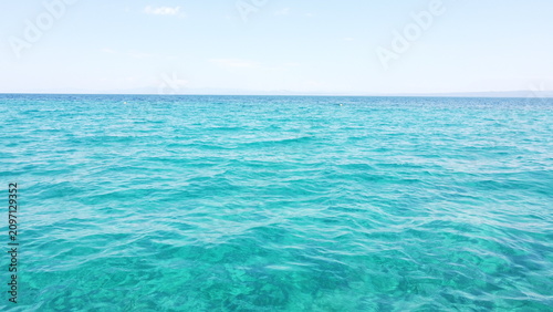 Turquoise sea water surface texture with small waves under clear horizon and sky