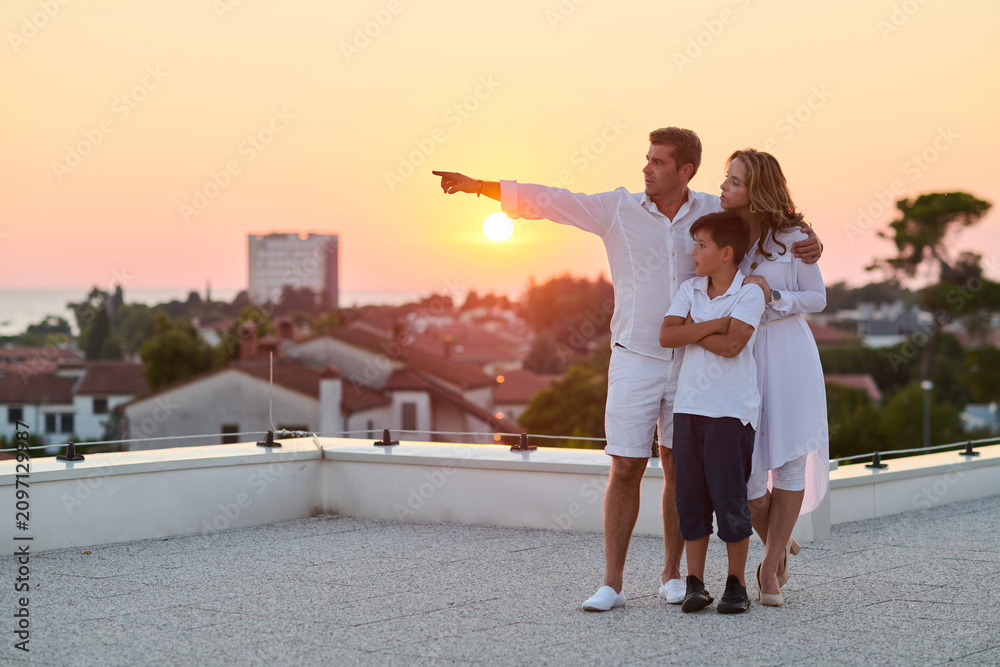 Obraz premium Family on Rooftop Terrace at Sunset Overlooking Sea View and Coastal Town