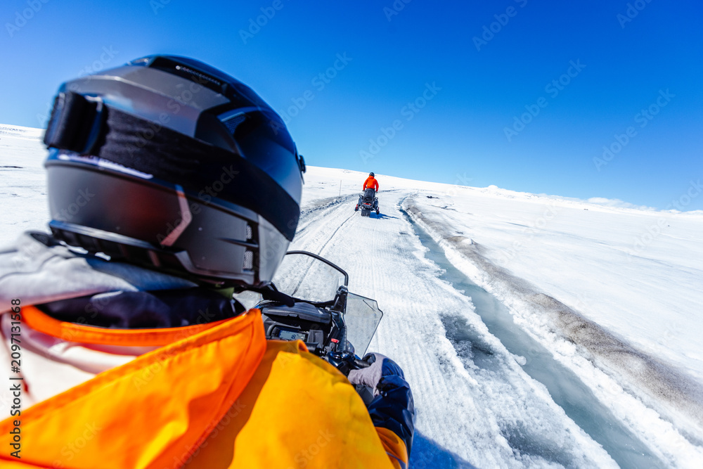 Obraz premium First-person view of a snowmobile tour across a vast Icelandic glacier. Adventure travel through pristine snowfields beneath a dramatic blue sky with wispy clouds in Iceland.