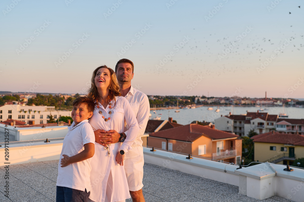 Obraz premium Happy Family On Rooftop Terrace With Sea View At Sunset Over Coastal Town