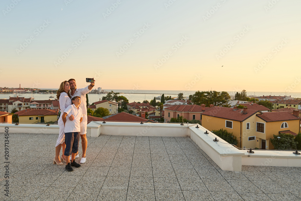 Obraz premium Family Taking Selfie on Rooftop Terrace With Sea View at Sunset During Vacation