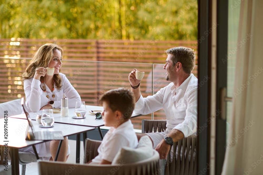 Obraz premium Family Enjoying Morning Coffee on Terrace Balcony While Relaxing and Conversing Together