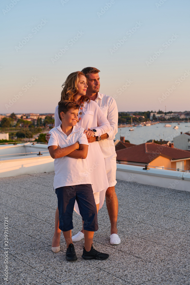 Obraz premium Family on Rooftop Terrace With Sea View at Sunset — Parents and Son Embracing on Balcony