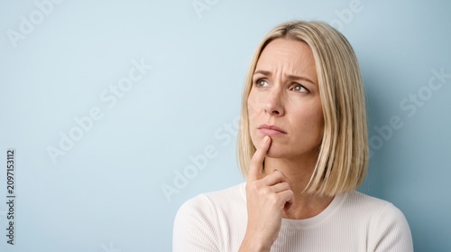 Thoughtful young blonde woman with a pensive expression looking up, contemplating a decision.