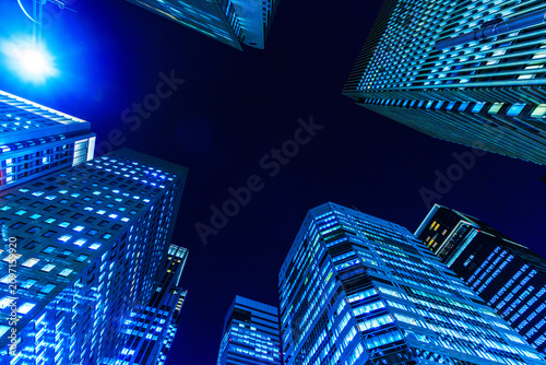 Futuristic cyber-blue city skyline of Tokyo's financial district from a dynamic looking-up perspective.