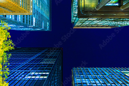 Futuristic cyber-blue city skyline of Tokyo's financial district from a dynamic looking-up perspective.