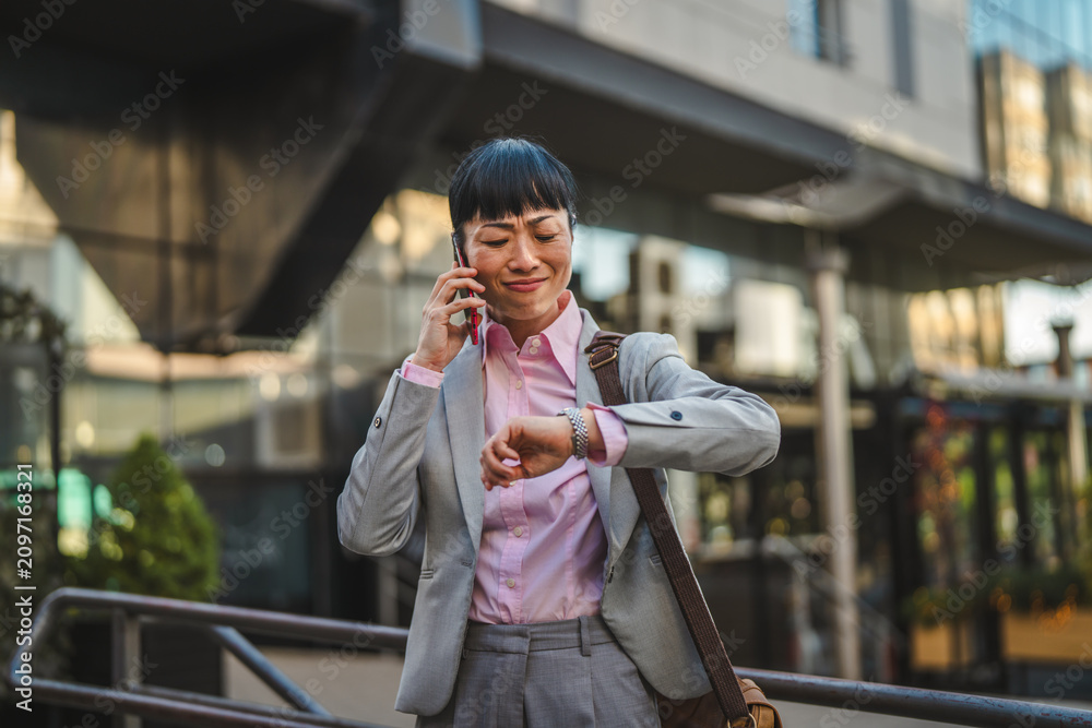 Fototapeta premium Stressed businesswoman talking on phone checking time