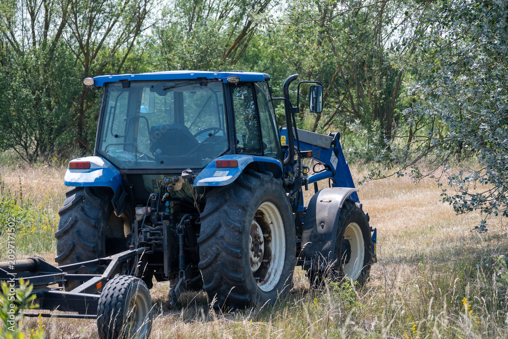 Obraz premium Blue tractor mowing grass in a rural field