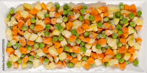 Canvas-taulu Top view of frozen mixed vegetables with peas, diced carrots, and potatoes covered in frost crystals on a white plate, healthy food ingredient and meal preparation concept