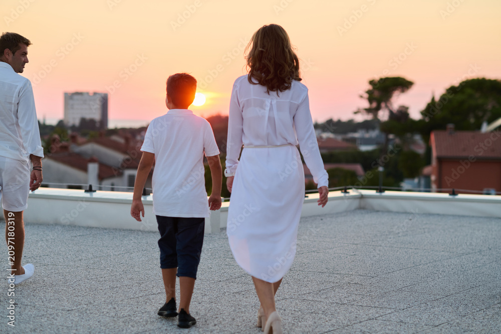 Obraz premium Family Walking on Rooftop Terrace at Sunset With Sea View on Summer Vacation
