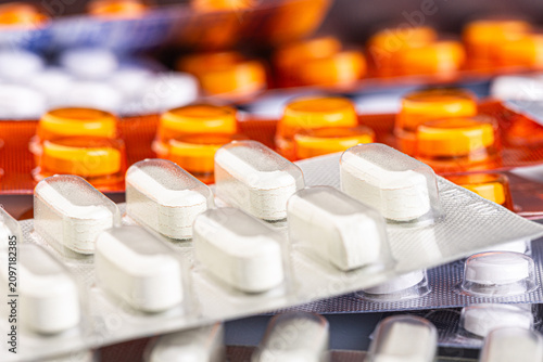 White caplets and orange tablets sit in blister packs on a clean surface. Healthcare concept for pharmacy, medication, treatment, and safe dosage.