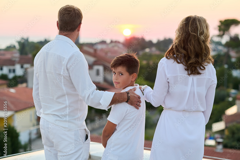 Obraz premium Family on Rooftop Balcony at Sunset With Sea View Parents and Son Embracing Outdoors