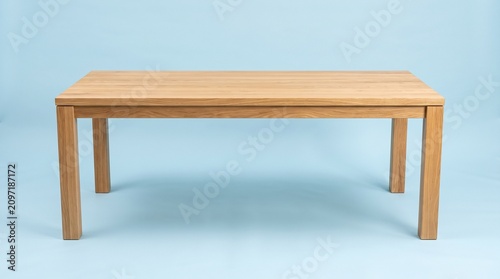 Minimalist rectangular wooden dining table made of light oak, featuring clean lines and a modern design, isolated against a solid light blue background.