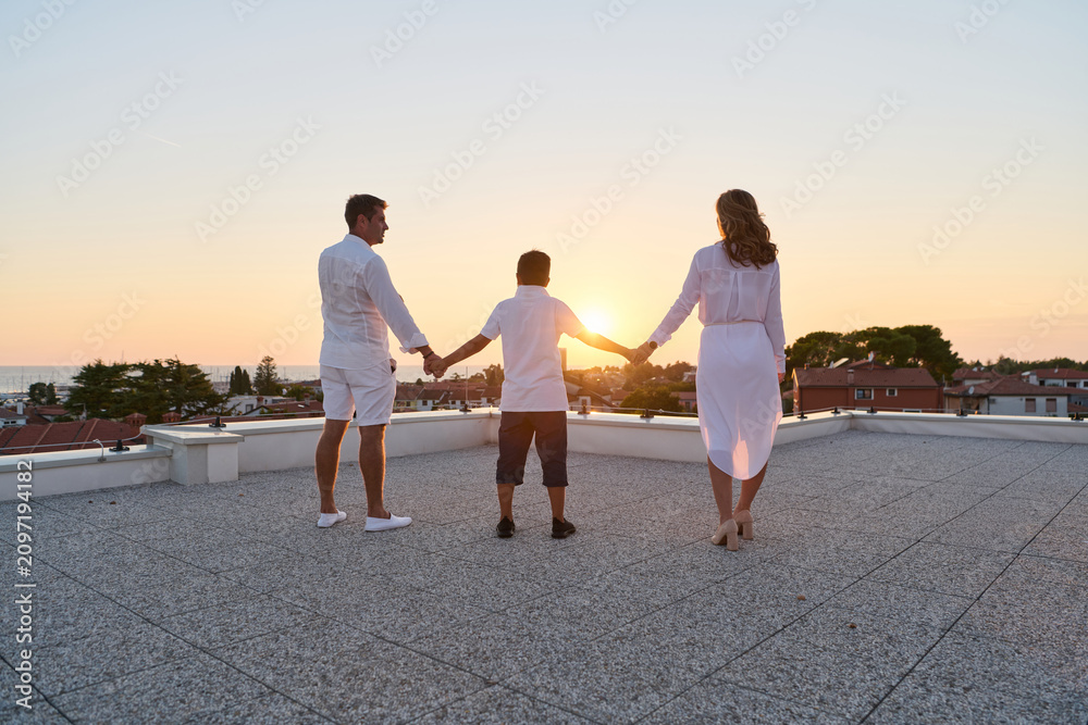 Obraz premium Family On Rooftop Terrace Holding Hands At Sunset With Sea View And Summer Vacation Feeling