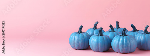 Decorative blue pumpkins placed against a soft pink studio background with ample text space offer a modern autumnal style and seasonal banner concept