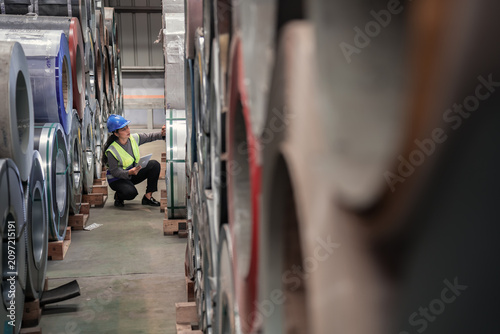 Bild auf Leinwand Technician Inspects Steel Rolls in Industrial Warehouse Setting