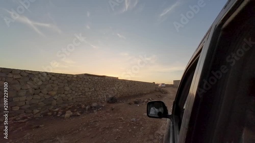 Car on rocky dirt road beside village at sunset. Socotra, Yemen.