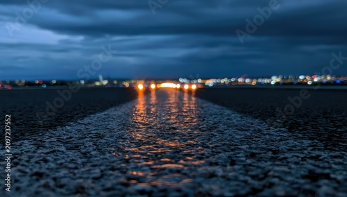 Wet road at dusk, reflecting distant city lights and headlights