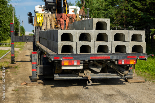 Crane truck carries precast concrete drainage channels on rural road. Concept: construction material delivery
