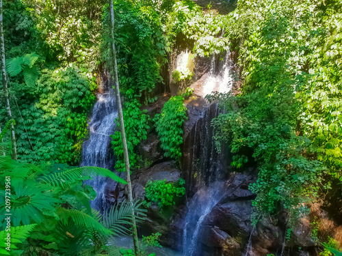Multiple tropical waterfalls cascading through dense jungle with Balinese temple shrine in background, Bali, Indonesia