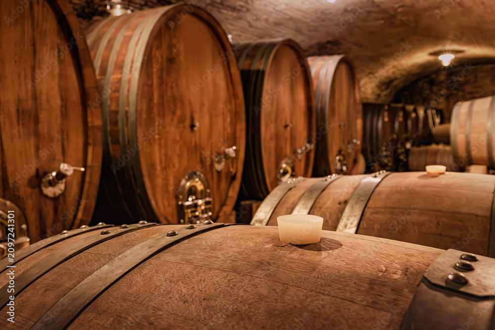 Obraz premium Wine barrels aging in a traditional underground cellar, showcasing the winemaking process and a rustic, authentic atmosphere