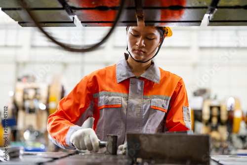 Factory worker in safety gear operating industrial machinery on a production line, focused on precision metalwork in a manufacturing plant.