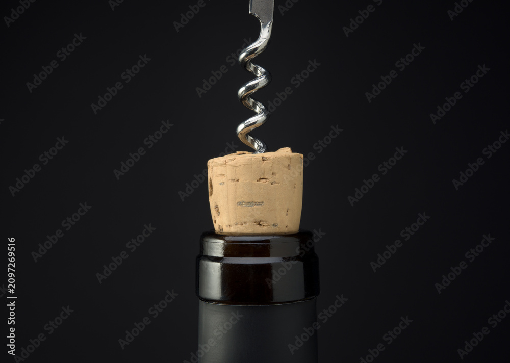 Obraz premium Uncorking a bottle of red wine close up, Opening wine bottle with corkscrew on dark background