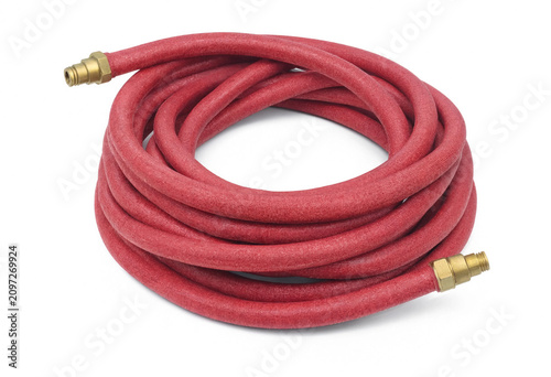Red flexible garden water hose coiled on white background with watering flexible irrigation equipment outdoors