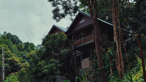 Wooden mountain cabins surrounded by lush tropical jungle on forest hillside, Scenic rainforest lodge retreat with elevated architecture, Mae Kampong Thailand 4k