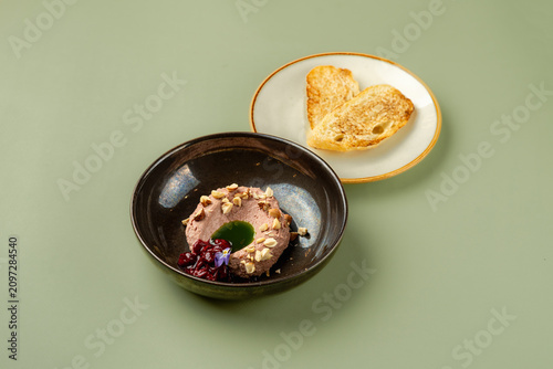 A round dessert sits in a dark bowl. It has garnishes on top. Next to it is a plate with two pieces of golden toast. The setting shows a plain table