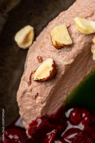 A dessert is placed in a dark bowl. It has a smooth texture and is topped with almond pieces. Cherry sauce is drizzled around the dessert, adding a sweet touch