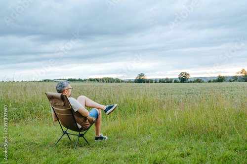 Middle aged man resting in folding chair surrounded by green countryside