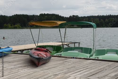 Red kayaks and catamarans on a wooden pier on a lake.