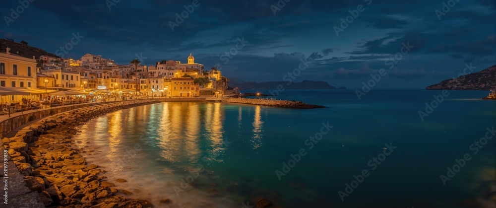 Naklejka premium Coastal Town Illuminated at Night with Reflections on Water