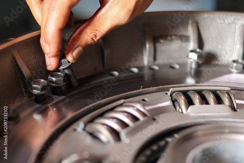 Obraz na plátně Close up of mechanic hand inserting a metal bolt into a heavy vehicle clutch pressure plate assembly before tightening in a workshop