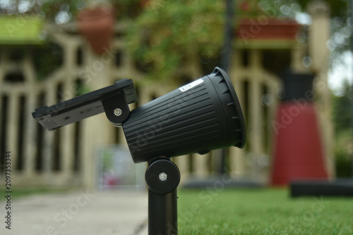 Closeup of a waterproof solar LED garden spotlight covered with rain drops beside bamboo plants. Eco friendly outdoor lighting for gardens, pathways and landscaping.
