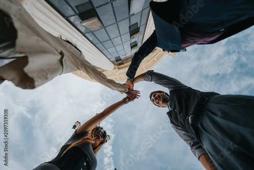 Quadro su tela A diverse business team stands outdoors and joins hands above their heads in a team gesture