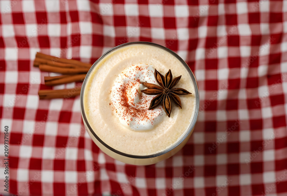 Fototapeta premium Top view of eggnog with whipped cream and star anise on plaid tablecloth