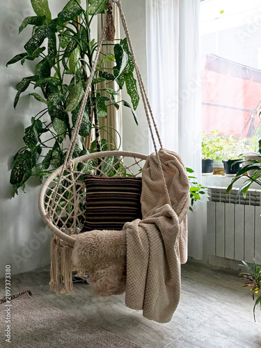 A modern cozy beautiful room with a braided rope macrame chair, green plants and a window with curtains. Interior and background. Location for photo shooting