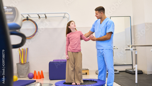 Child physiotherapy session, therapist assisting girl on trampoline for balance training, pediatric rehabilitation exercises in clinic, physical therapy session, motor skills development