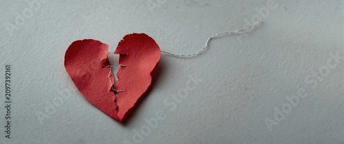 Top view of a ripped crimson paper heart sewn together with thread on a pale grey surface