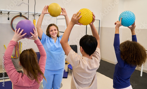Pediatric physiotherapy session with therapist and children doing exercises with colorful balls, rehabilitation and motor skills training in pediatric rehab center