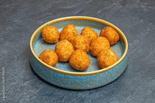 Crispy golden ham croquettes revealing a creamy interior, served on a blue and grey ceramic plate over a dark surface.